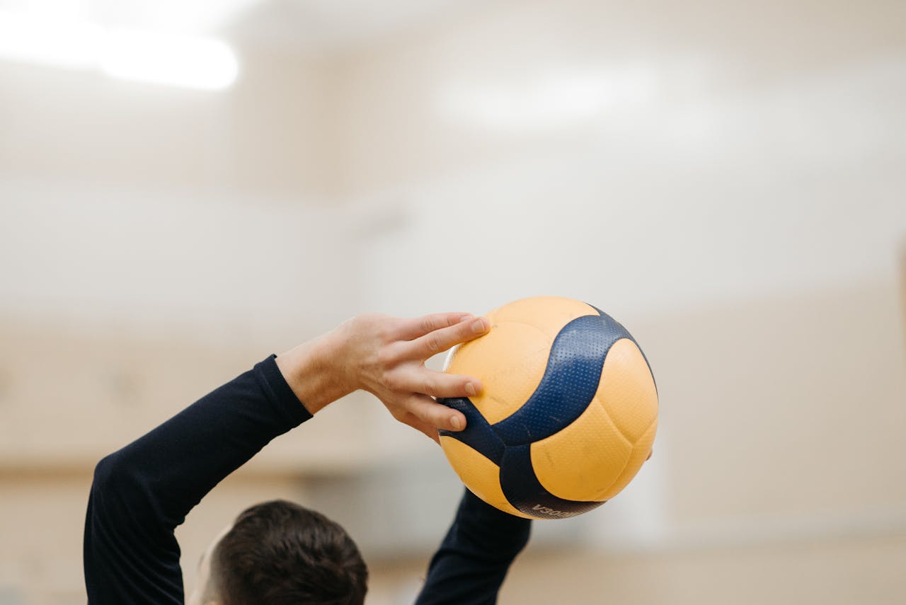 Close-up of a volleyball player holding a ball overhead, ready to serve in a gymnasium.